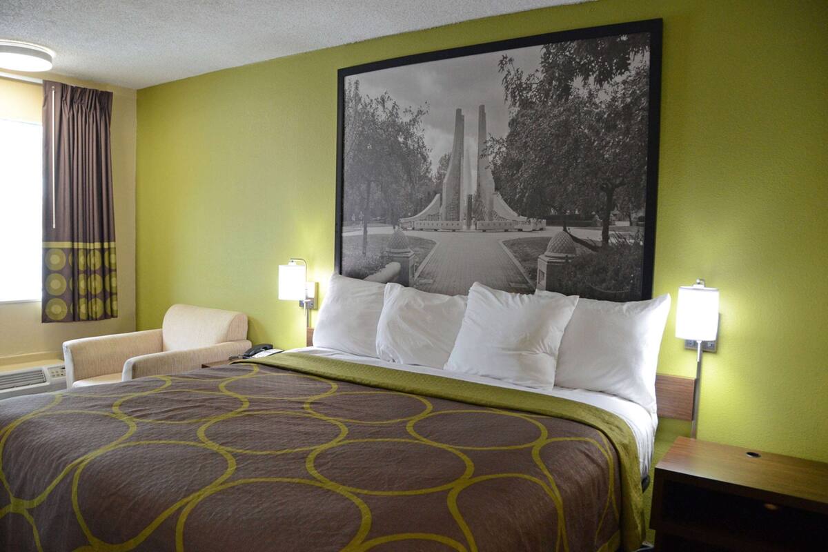 Une chambre d’hôtel avec un grand lit, une chaise et une lampe fixée au mur.
