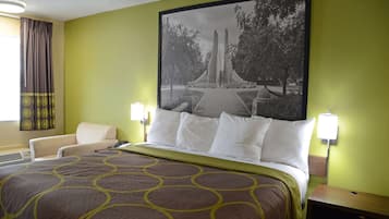 A hotel room with a large bed, a chair, and a wall-mounted lamp.