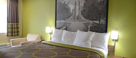 A hotel room with a large bed, a chair, and a wall-mounted lamp.