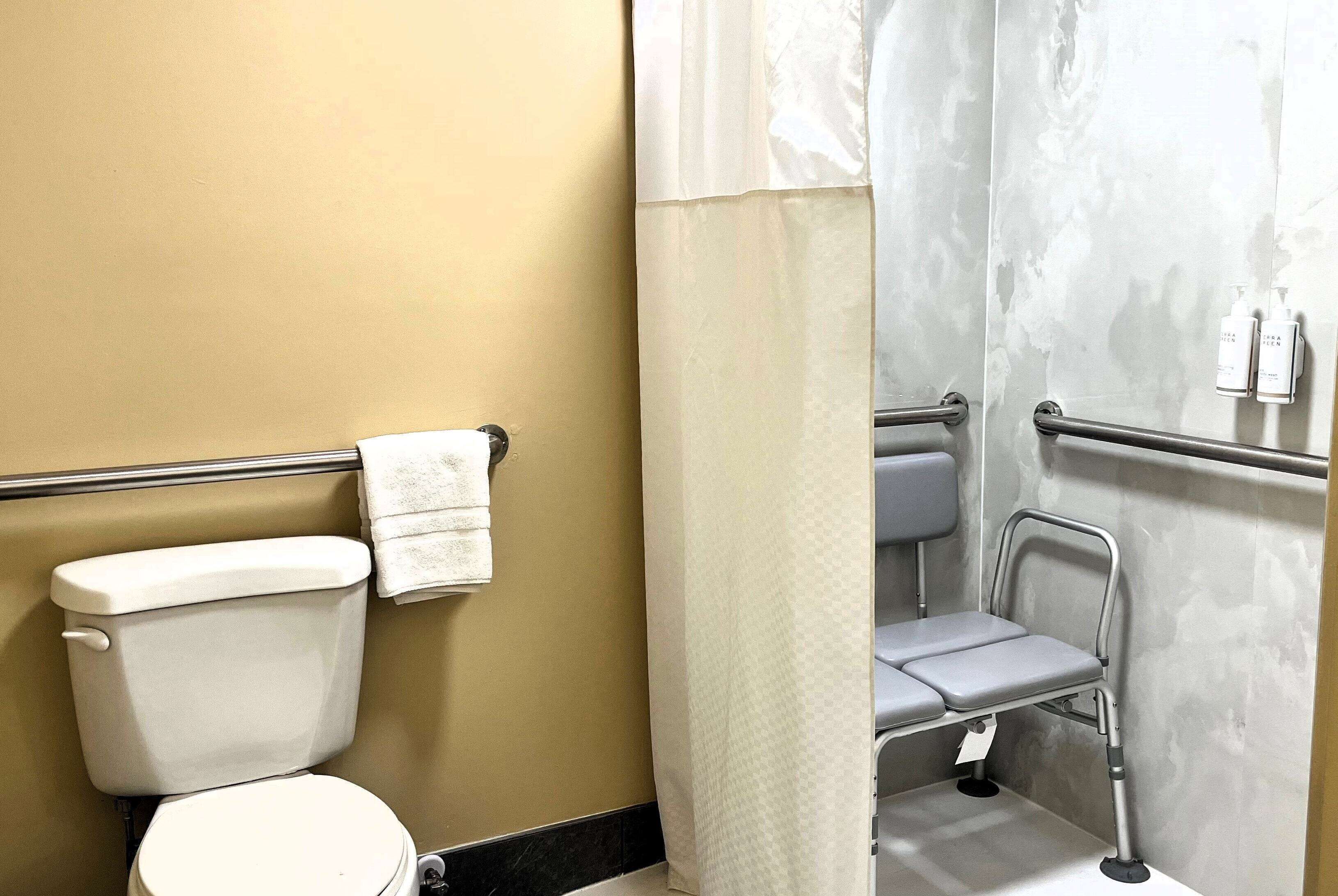 A bathroom with a toilet, a shower with a grab bar, and a towel hanging on the wall.