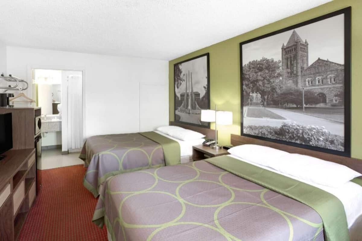 Une chambre d’hôtel avec deux lits, un bureau, une chaise, un miroir et une porte donnant sur une salle de bain.