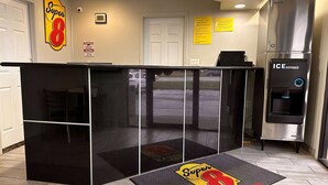 A hotel reception area with a black counter, a Super 8 logo on the wall, and an ice dispenser. - Super 8 by Wyndham Lafayette / Purdue Area (Lafayette)