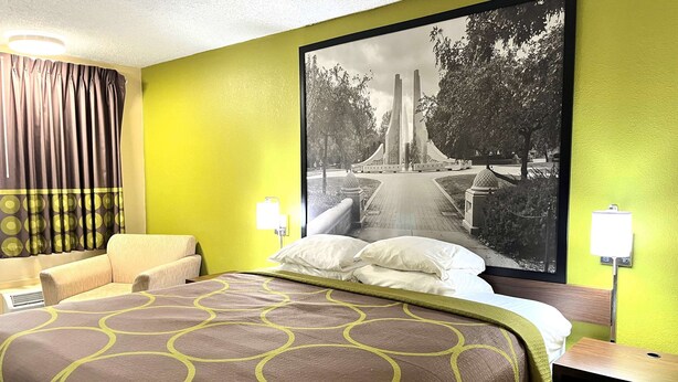 A hotel room with a large bed, a sofa, a wall-mounted TV, and a poster of a park. - Super 8 by Wyndham Lafayette / Purdue Area (Lafayette)