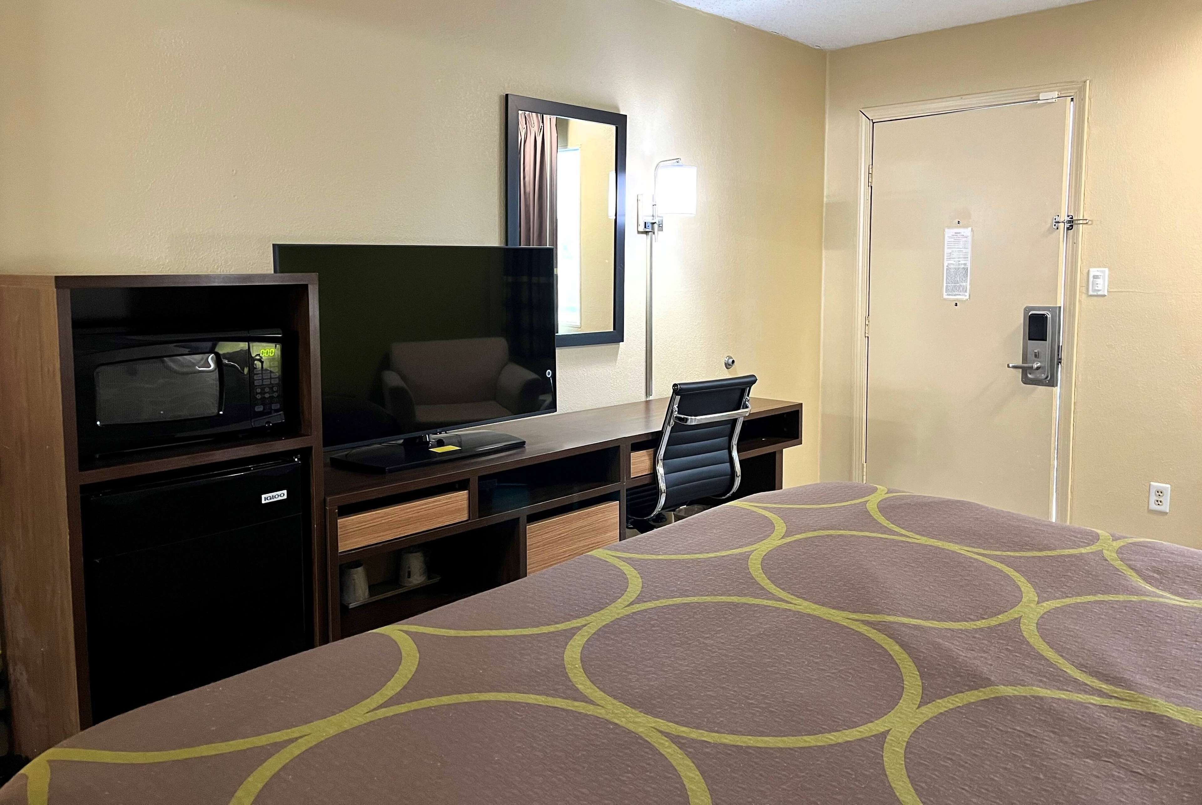 A hotel room with a bed, a desk with a computer, a microwave, and a chair.