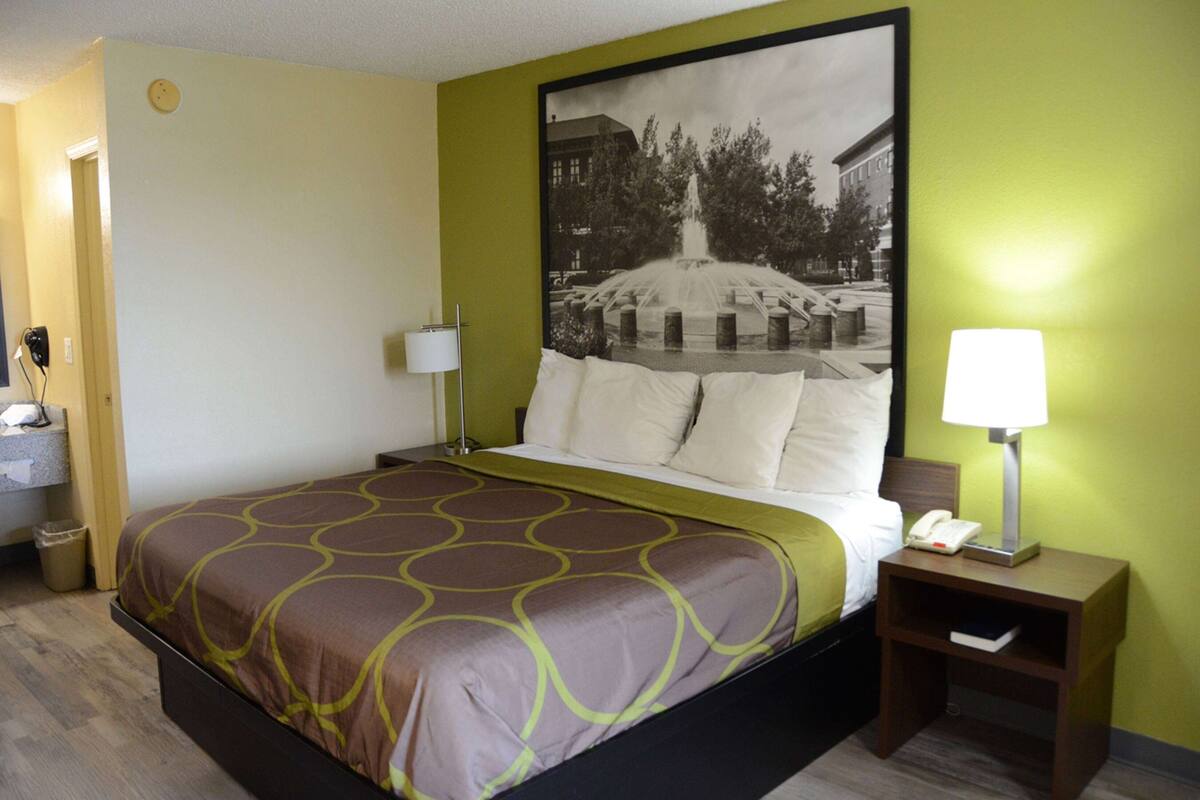 Une chambre d’hôtel comprenant un lit, deux tables de chevet, une commode, une lampe, un téléphone et un tableau accroché au mur.