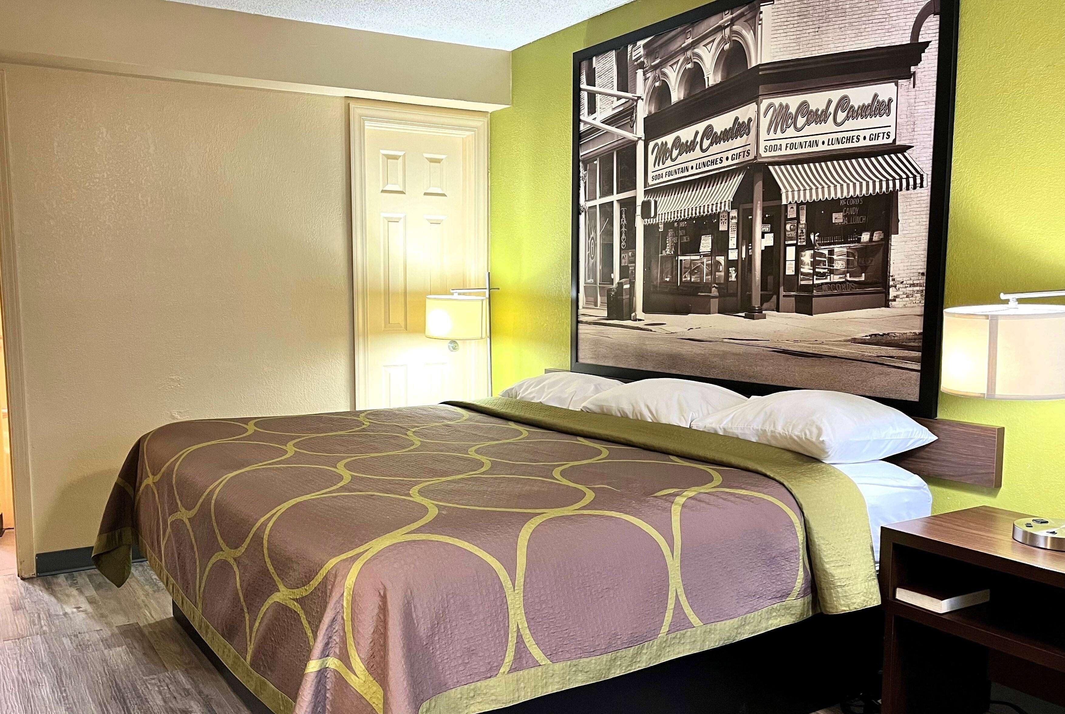 A hotel room with a bed, a nightstand, a lamp, and a wall-mounted TV.