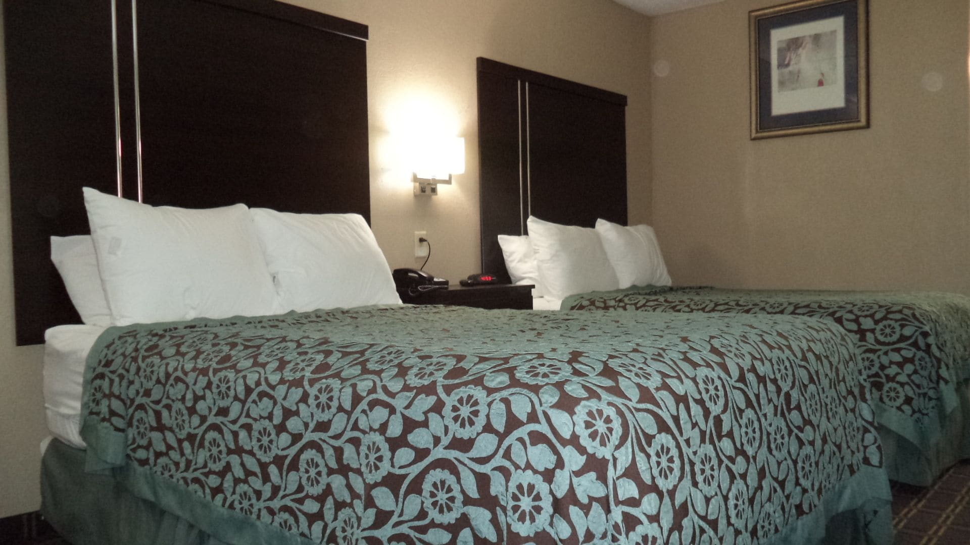 A hotel room with two beds, a nightstand, a lamp, and a framed picture on the wall.