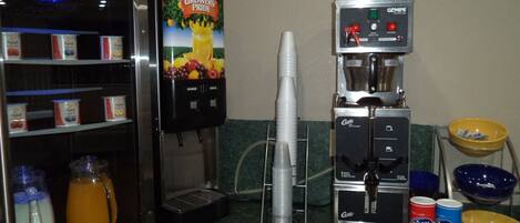 A self-serve coffee station with a beverage dispenser, a juice dispenser, and a selection of condiments and utensils.