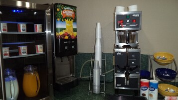 Una estación de café autoservicio con dispensador de bebidas, dispensador de jugo y una variedad de condimentos y utensilios.