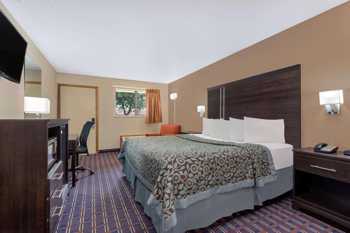 A hotel room with a bed, a desk, a chair, a TV, and a window with curtains.