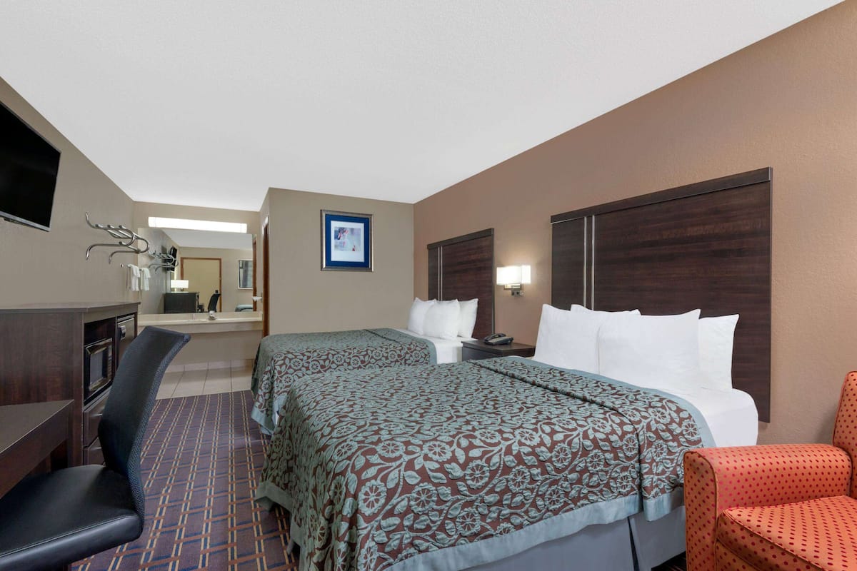 A hotel room with two beds, a desk, a chair, a TV, and a bathroom in the background.