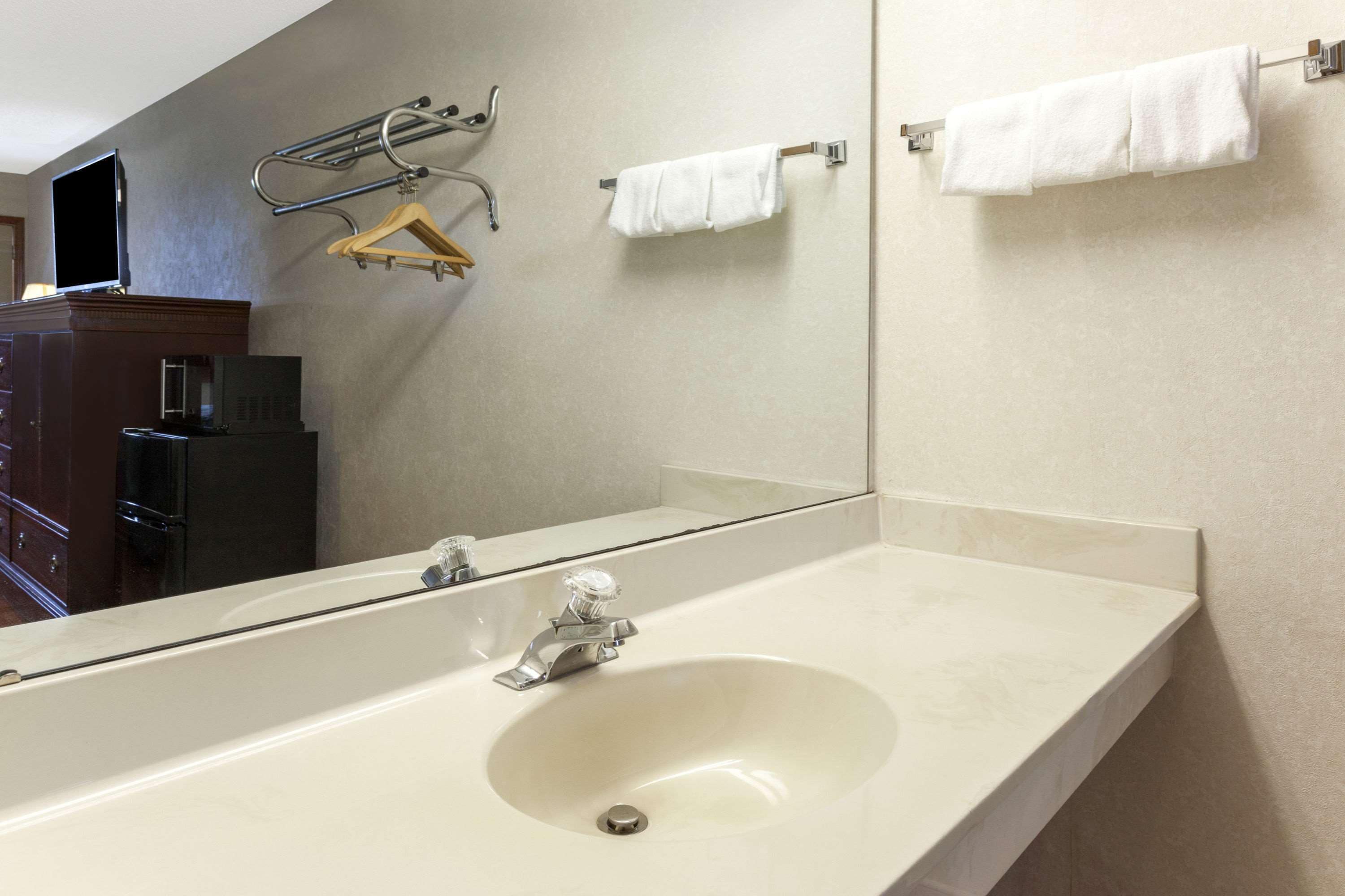 A bathroom with a large mirror, a sink, and towel racks.