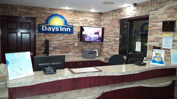 Een receptiebalie met een Days Inn bord, een televisie, een printer en een plaquette aan de muur.