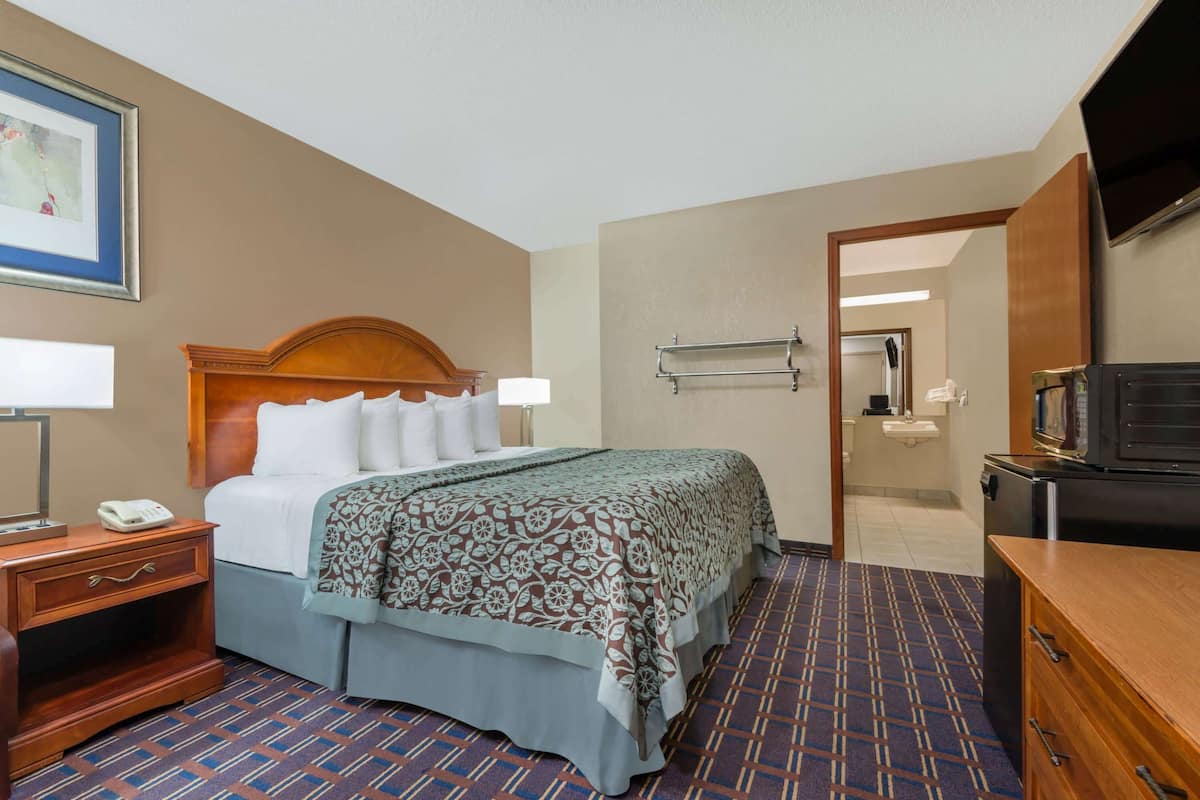 A hotel room with a bed, bedside table, lamp, TV, and a bathroom visible through an open door.