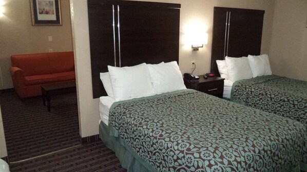 A hotel room with two beds, a sofa, a nightstand, and a wall-mounted light.