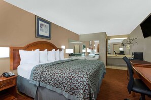 A hotel room with a bed, bedside table with a phone, a desk with a chair, a TV, and a mirror.