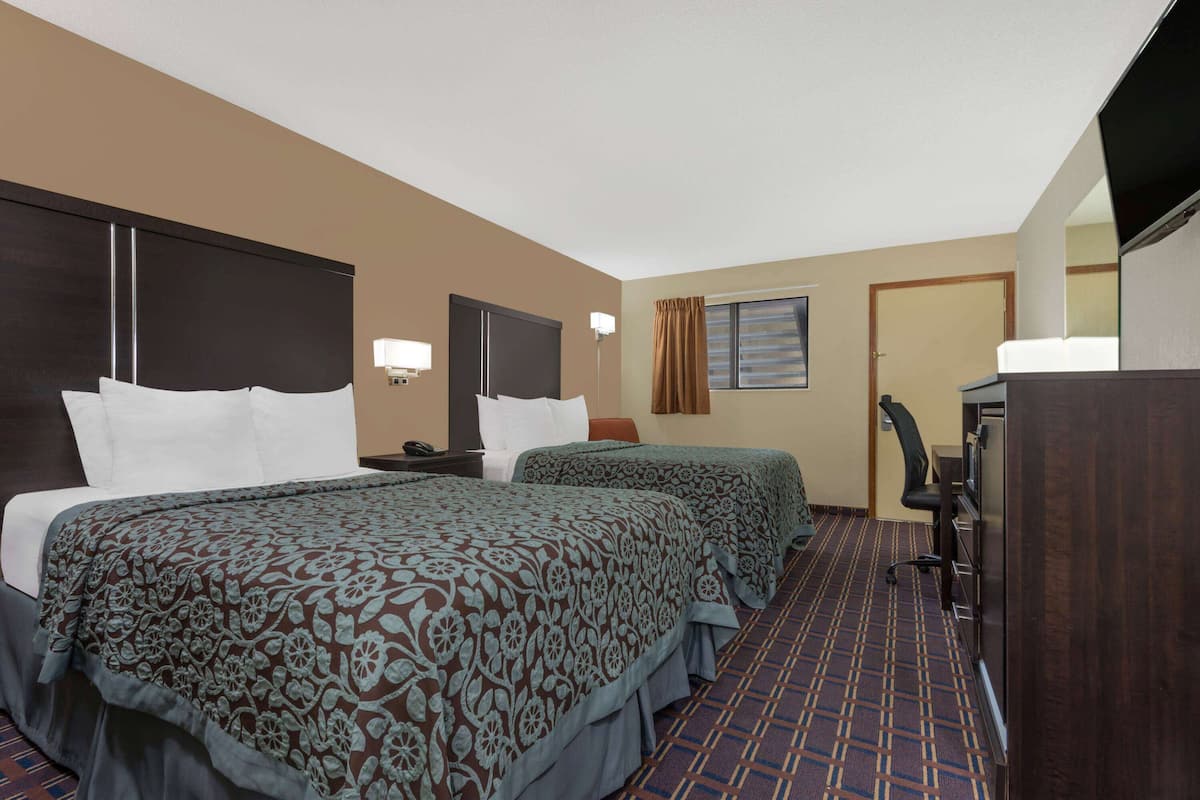 A hotel room with two beds, a desk, a chair, a TV, and a window with curtains.
