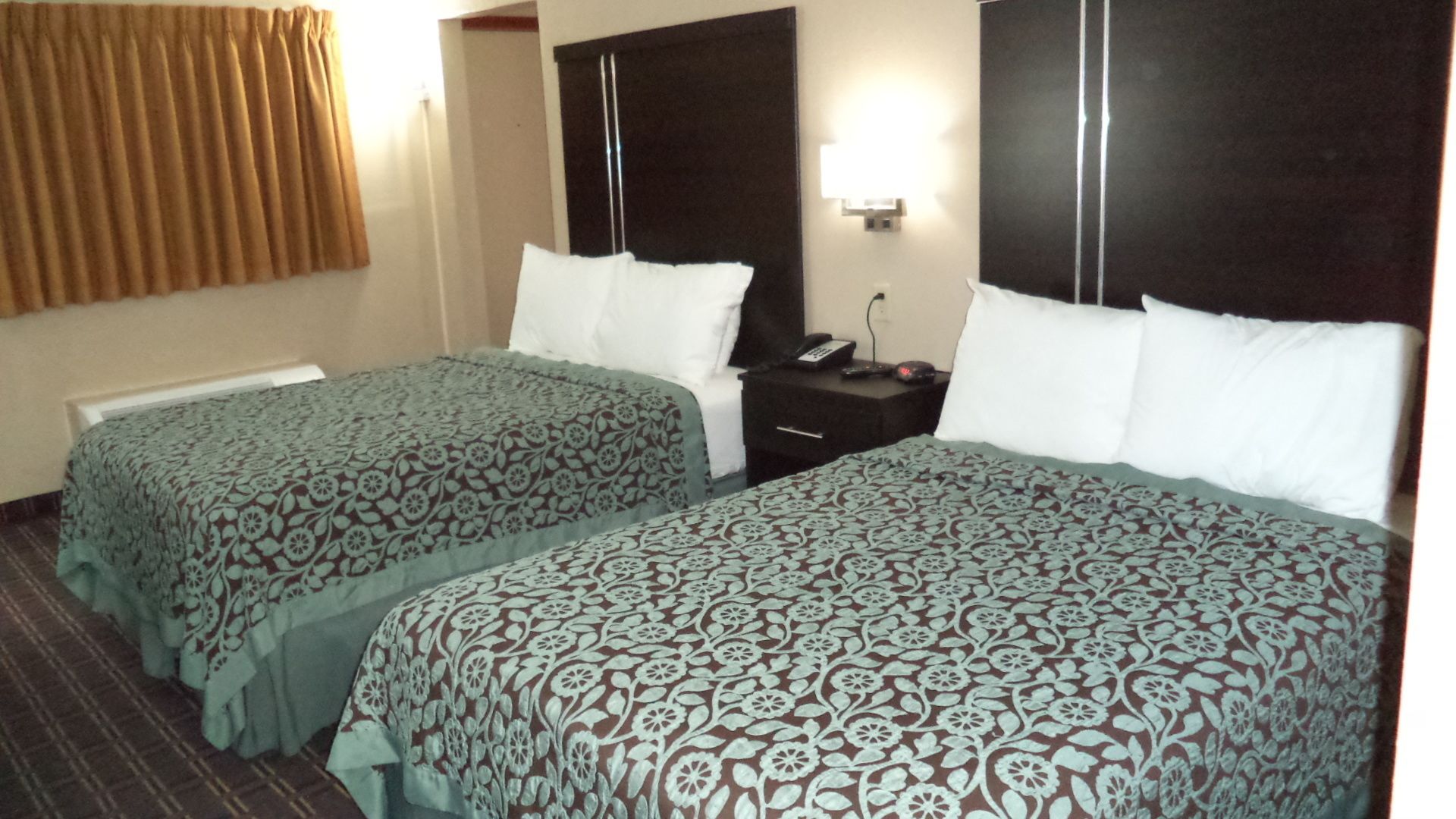 A hotel room with two single beds, a nightstand with a phone, and a wall-mounted light.