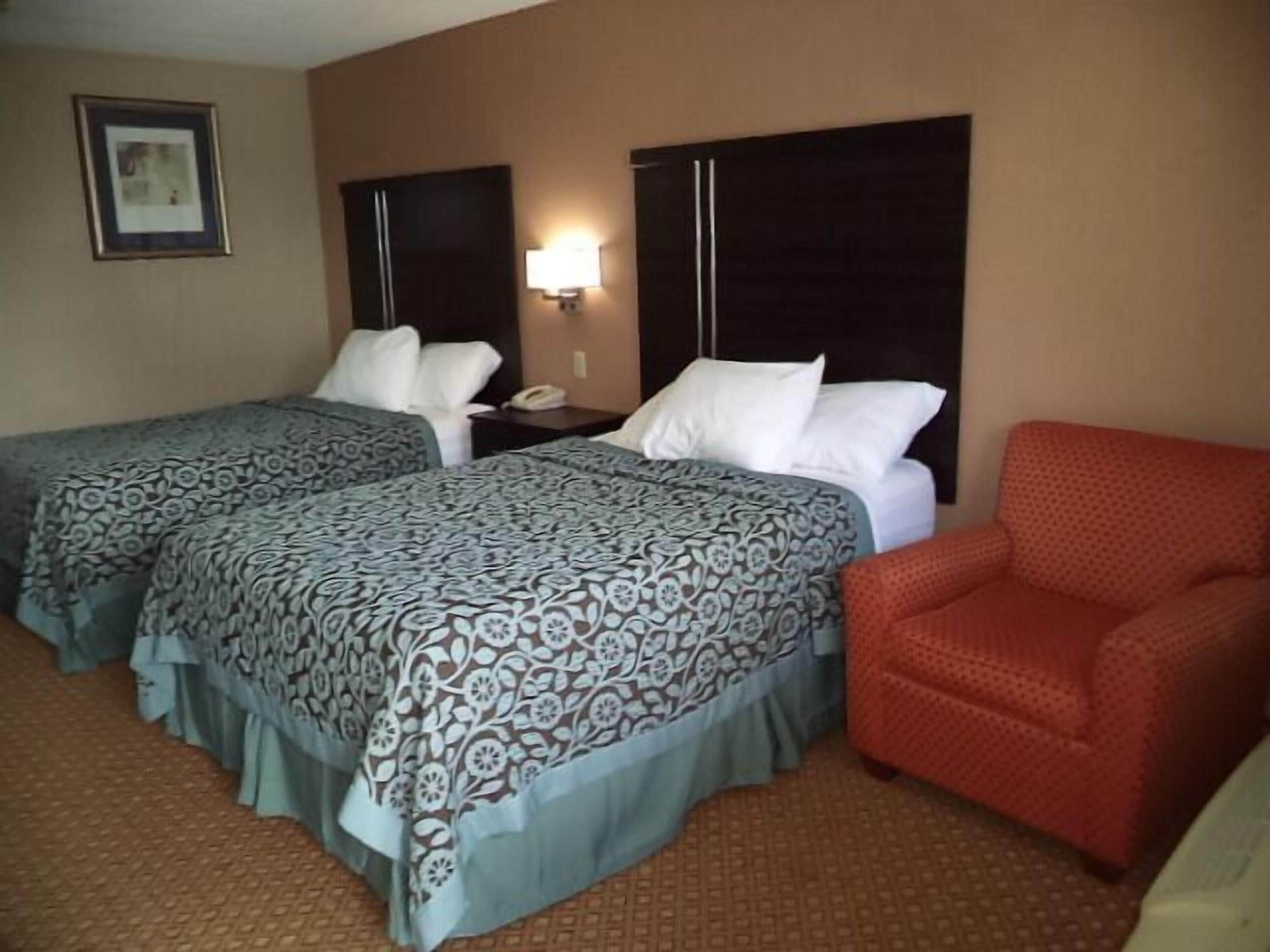 A hotel room with two beds, a nightstand, a red armchair, and a wall-mounted lamp.
