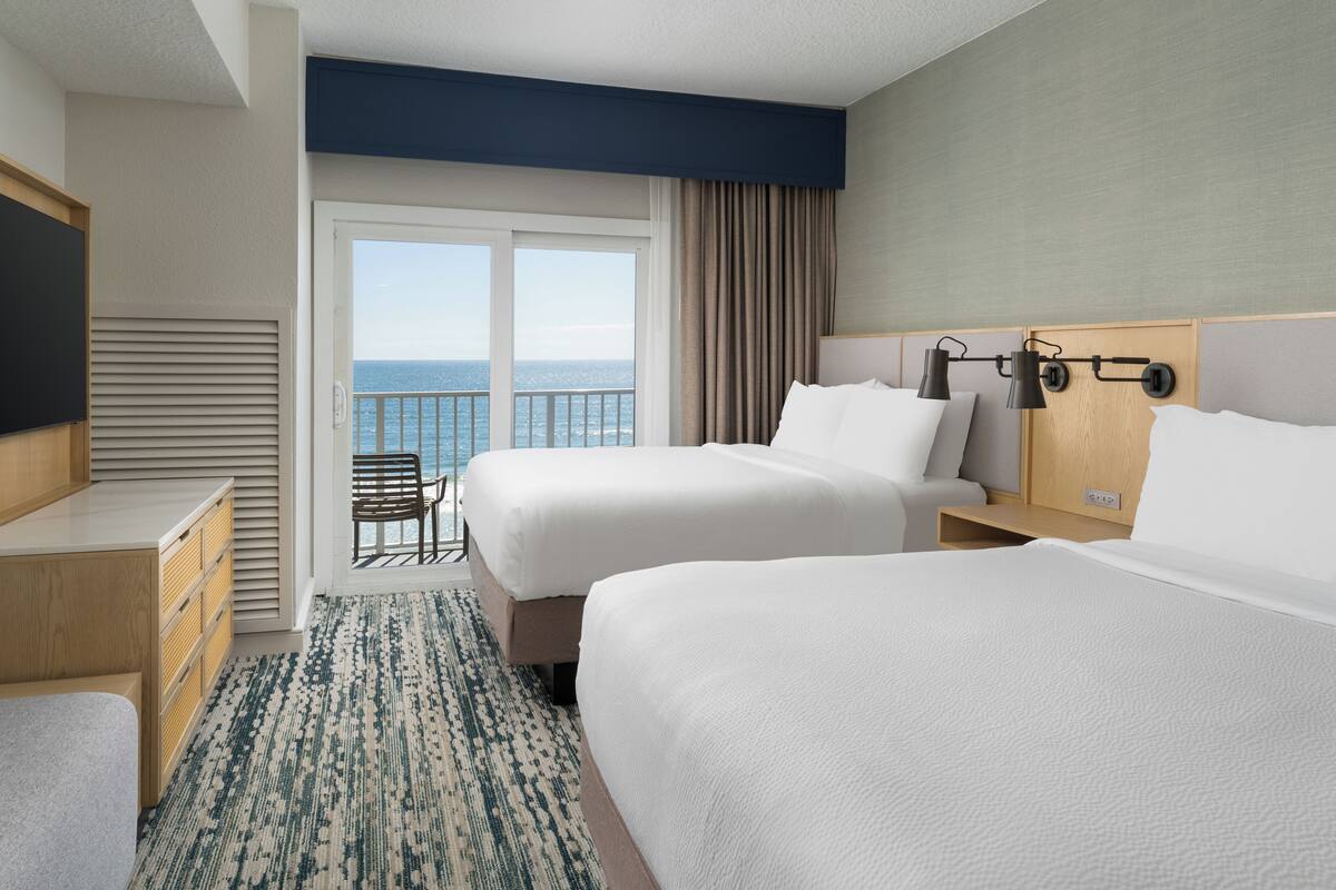 Habitación de hotel con dos camas, un escritorio, una silla y vista al océano.