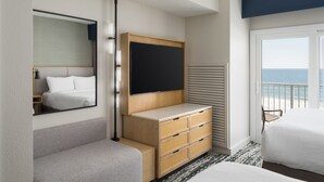 Een hotelkamer met een bed, een televisie, een houten dressoir, een spiegel en uitzicht op zee.