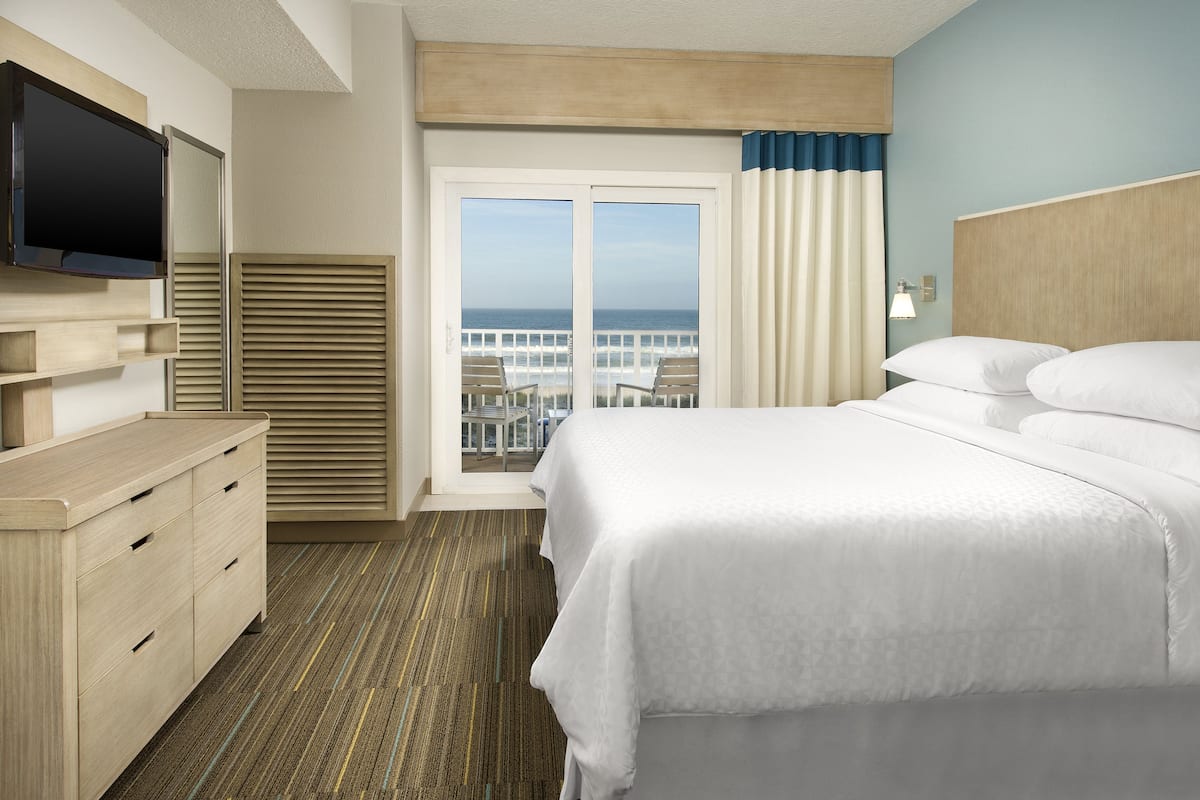 Una habitación de hotel con cama, televisión, escritorio y vista al océano.