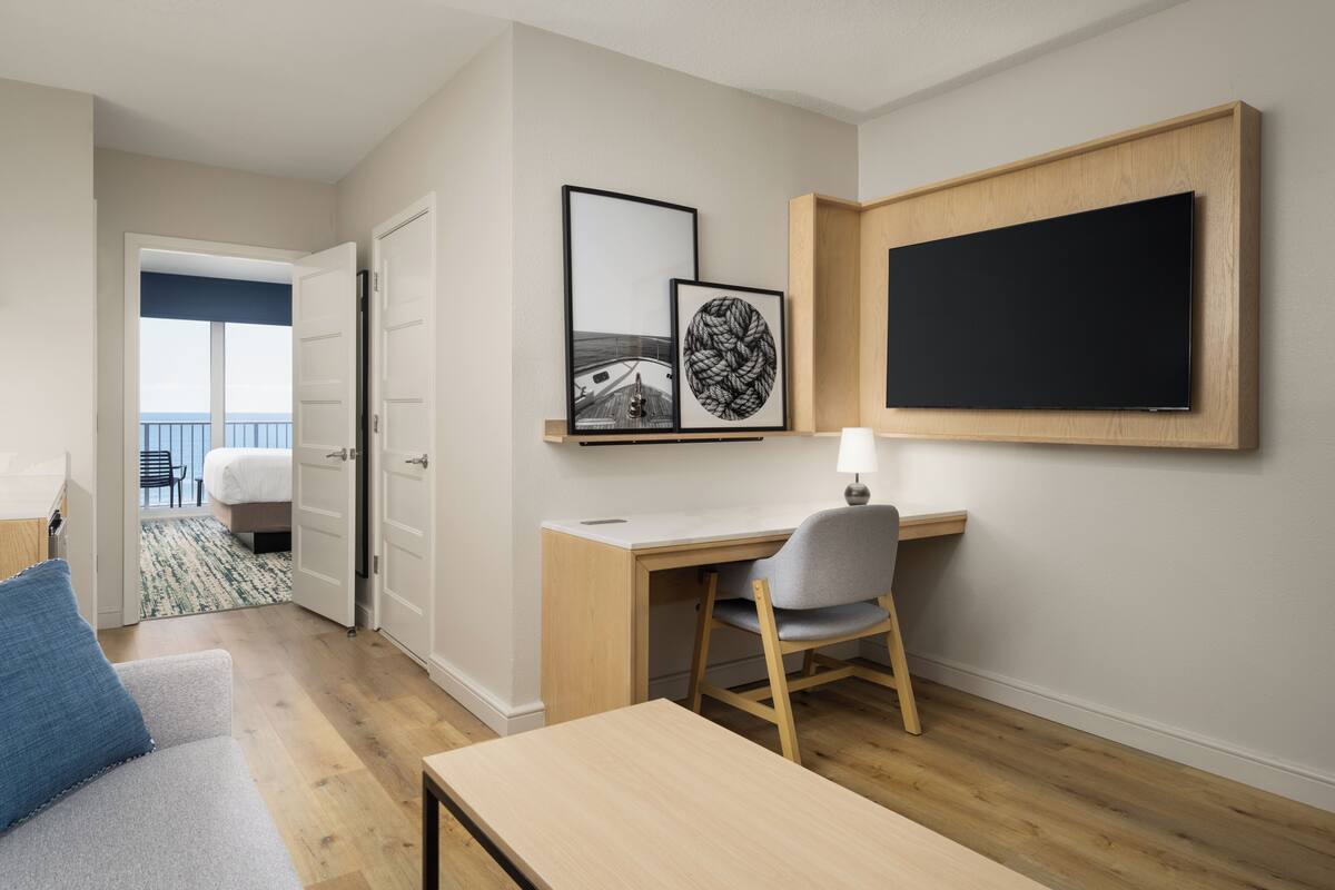 Una habitación de hotel moderna con escritorio de madera, una silla, una cama y un balcón con vistas.