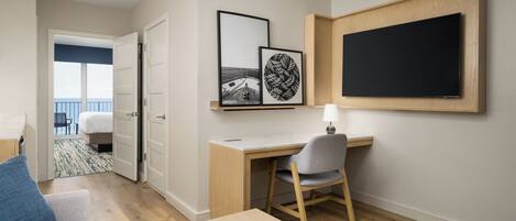 A modern hotel room with a wooden desk, a chair, a bed, and a balcony with a view.