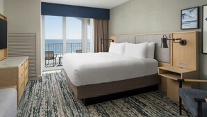 Een hotelkamer met een groot bed, een bureau, een stoel, een televisie en uitzicht op zee.
