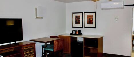 A hotel room with a bed, a desk with a chair, a television, a ceiling fan, and framed pictures on the wall.