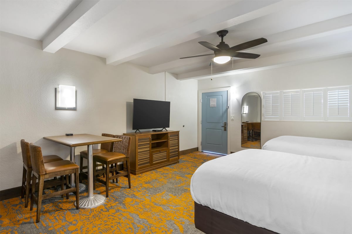 A hotel room with a bed, a desk with a chair, a television, and a ceiling fan.
