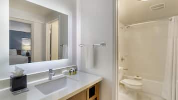 Un baño con un espejo grande, un lavabo con artículos de aseo, inodoro y ducha.