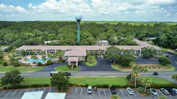 An aerial view of a hotel with a swimming pool, parking lot, and a tower.