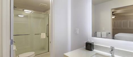 A modern bathroom with a glass-enclosed shower, a white toilet, and a sink with a mirror.
