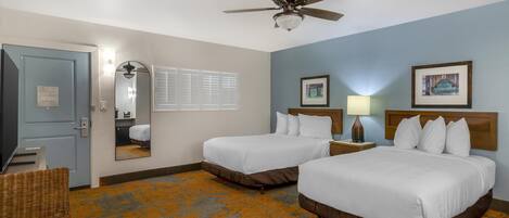 A hotel room with two beds, a ceiling fan, a television, a mirror, and a window with blinds.