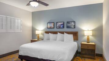 A hotel room with a bed, two bedside tables with lamps, a ceiling fan, and three framed pictures on the wall.