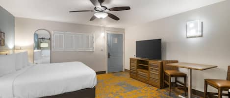 A hotel room with a bed, a desk, a television, and a ceiling fan.