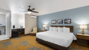 Une chambre d’hôtel comprenant un lit, un bureau, une chaise, un ventilateur de plafond et un mur orné de trois tableaux encadrés.
