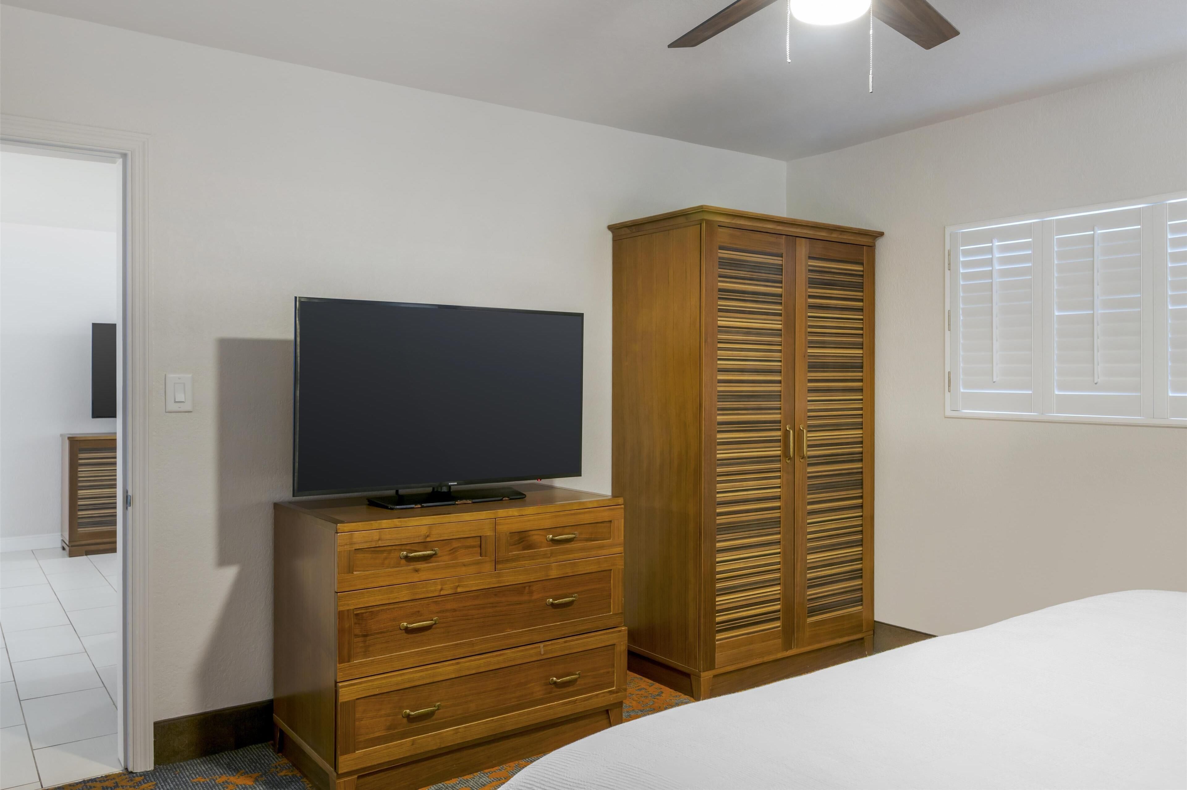 Un dormitorio con una cama, un televisor sobre un aparador de madera, un armario y una ventana con persianas.