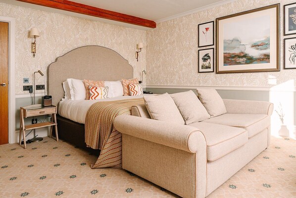 A bedroom with a bed, a sofa, a bedside table, a lamp, and framed artwork on the wall. - South Lodge (Horsham)