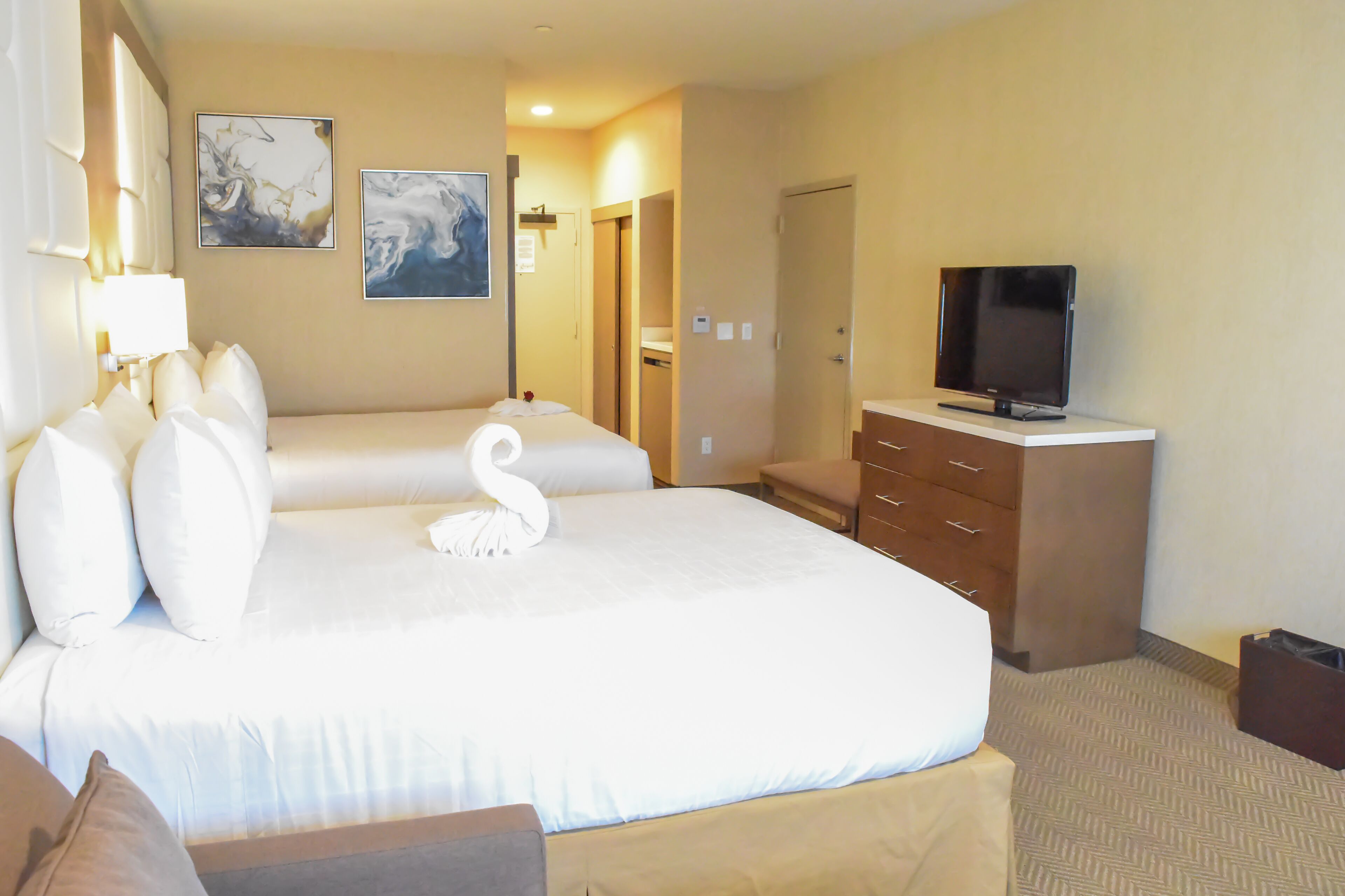 A hotel room with a large bed, a TV on a dresser, and artwork on the wall.