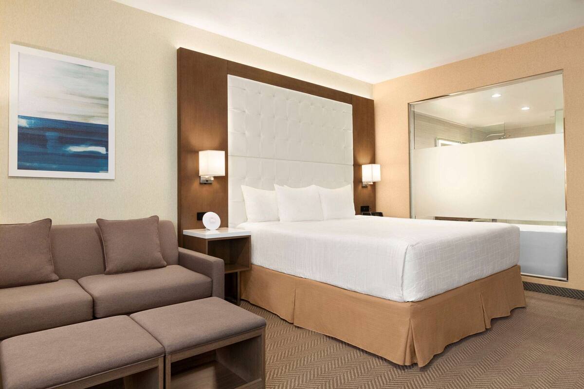 A hotel room with a large bed, a sofa, a nightstand, and a wall-mounted lamp.