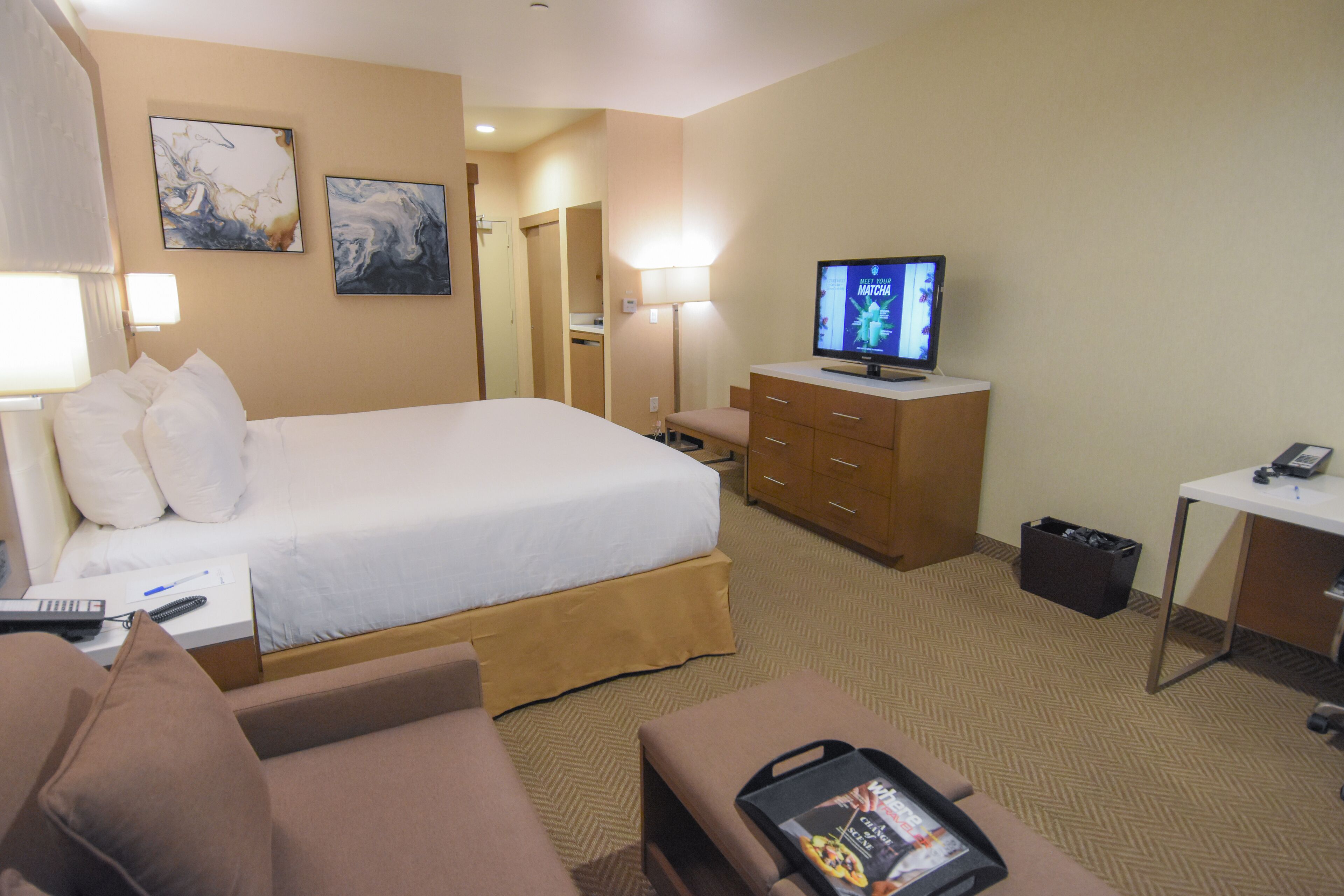A hotel room with a bed, a desk, a television, and a seating area.