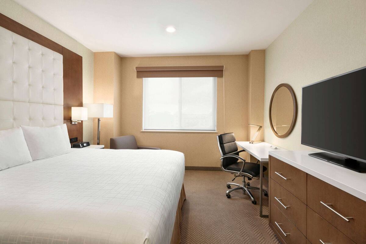 A hotel room with a large bed, a desk with a chair, a television, and a window with blinds.
