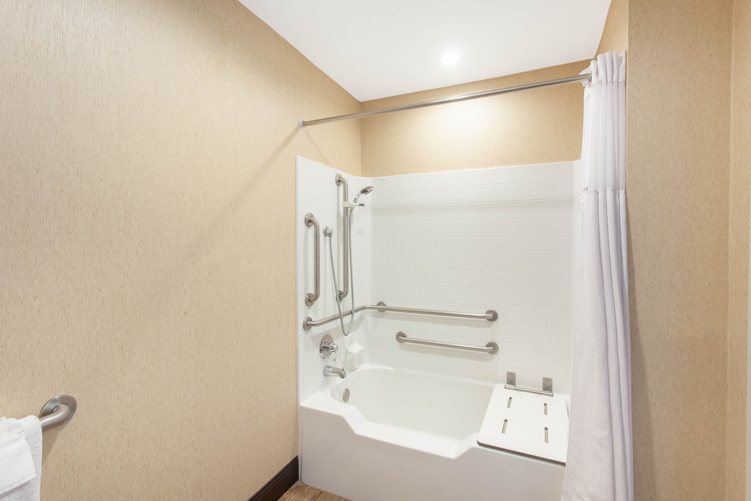 Un baño moderno con ducha a ras de suelo, barras de apoyo y una bañera blanca.