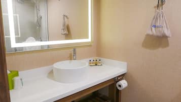 A bathroom with a white sink, a mirror with a light, a towel rack, and a toilet paper holder.