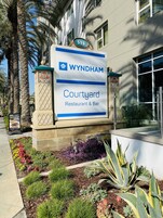 A sign for 'WYNDHAM Courtyard Restaurant & Bar' with a number '515' above it, surrounded by a landscaped garden with various plants and a palm tree.