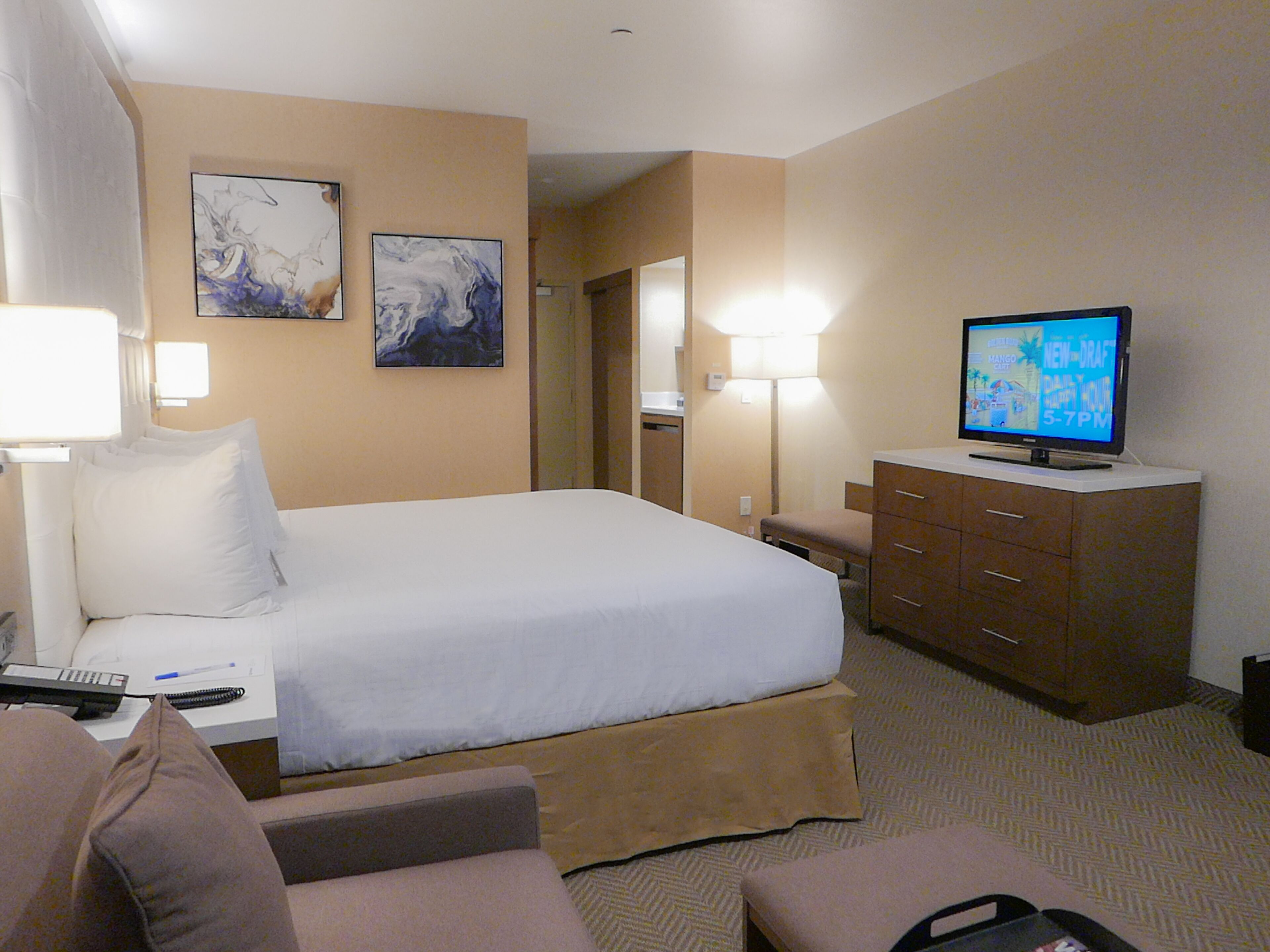 A hotel room with a bed, a desk, a television, and a dresser.