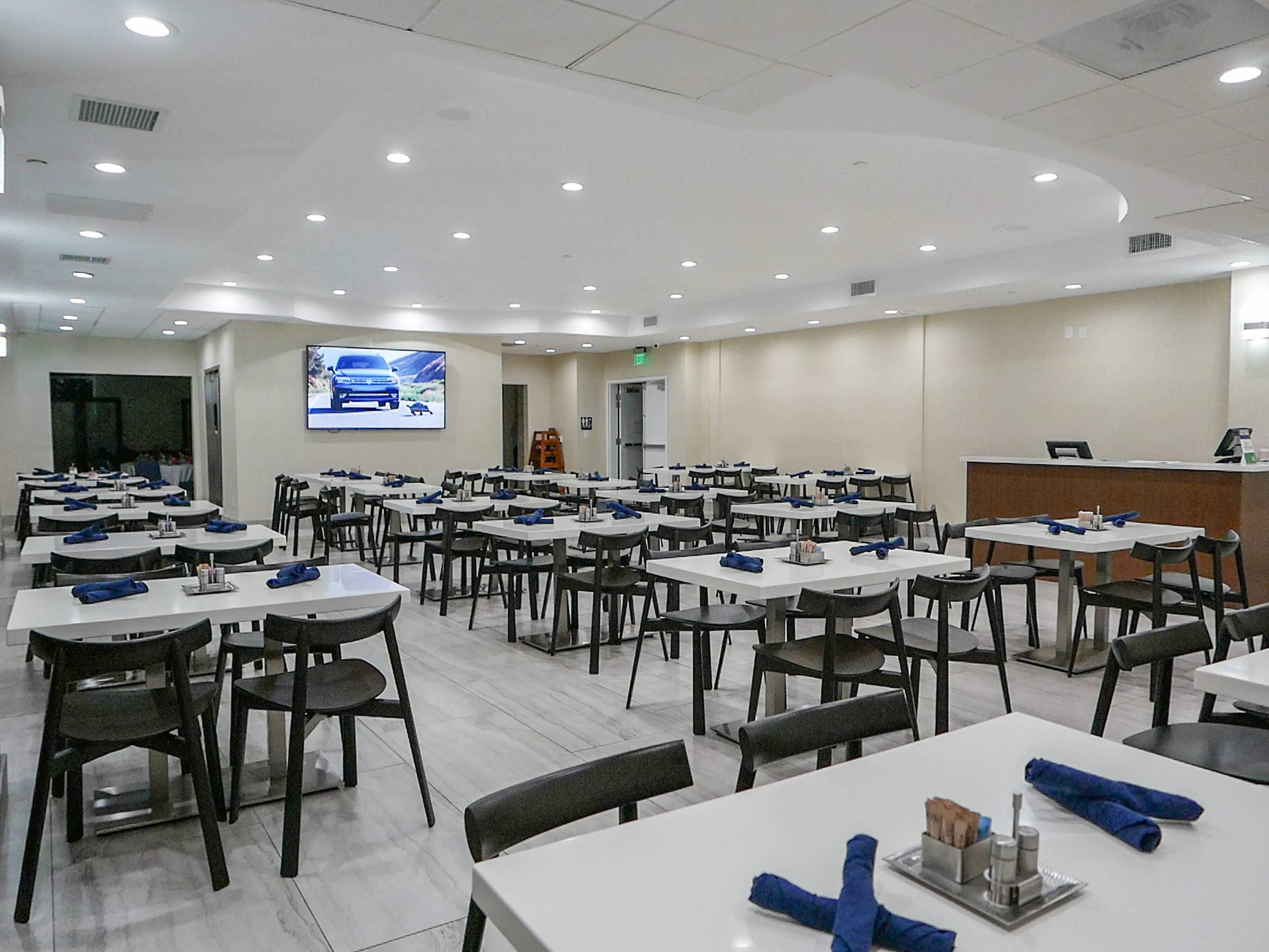 A conference room with multiple tables and chairs, a projection screen, and a reception desk.