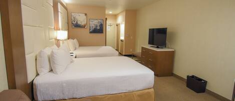 A hotel room with two beds, a TV, a dresser, and a trash bin.